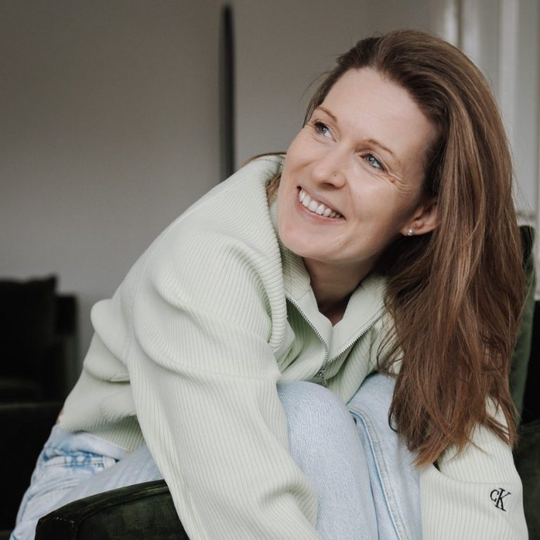 Kundinnen Feedback Kinderwunsch Coaching Schrörs Lächelnde Frau in heller, lässiger Kleidung sitzt auf einem Sofa.